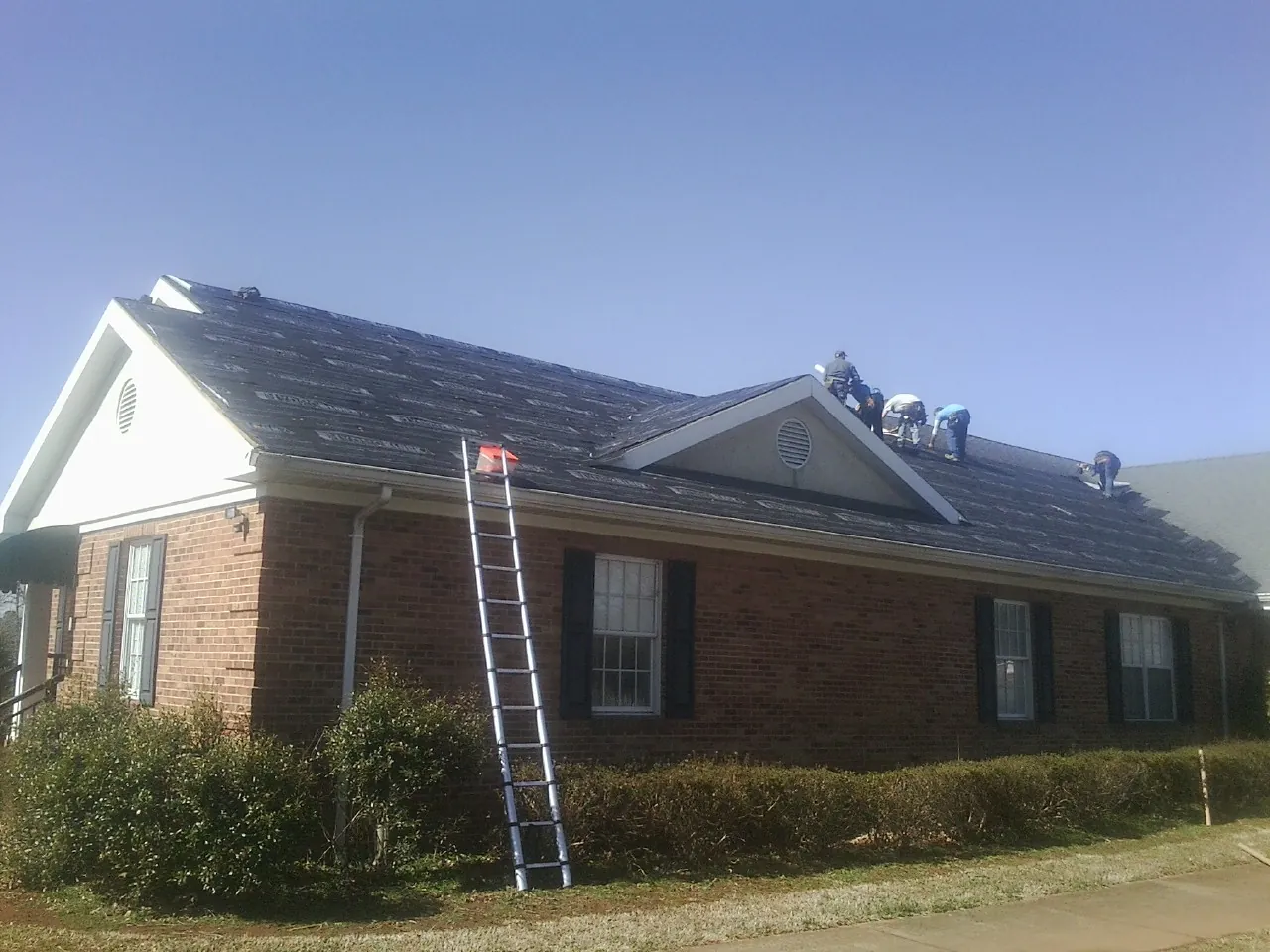 Crew tearing shingles off a brick ranch roof with a ladder set — Metal Roof Repair work by our crew in York Springs