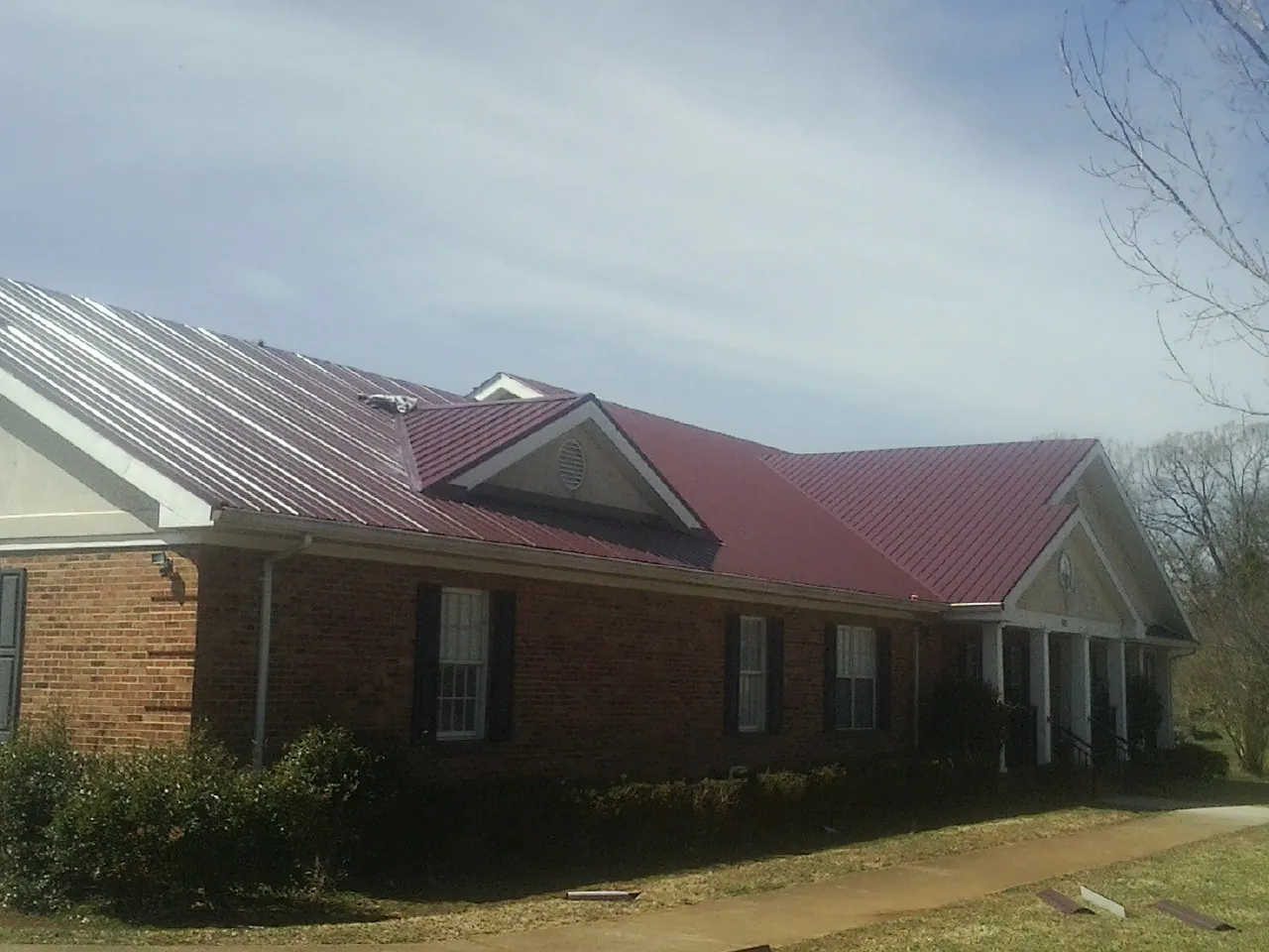 Red metal roof with gabled entries on a long brick building, from a Hail Damage Roof Repair job in York Springs