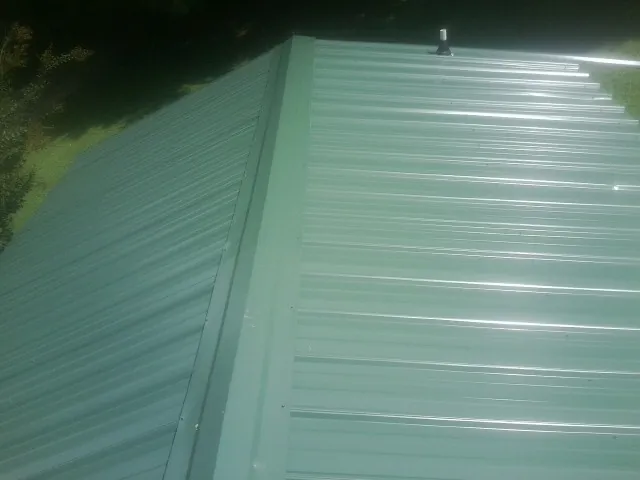New green metal panels meeting at the ridge of a roof — Flat Roof Repair work by our crew in York Springs