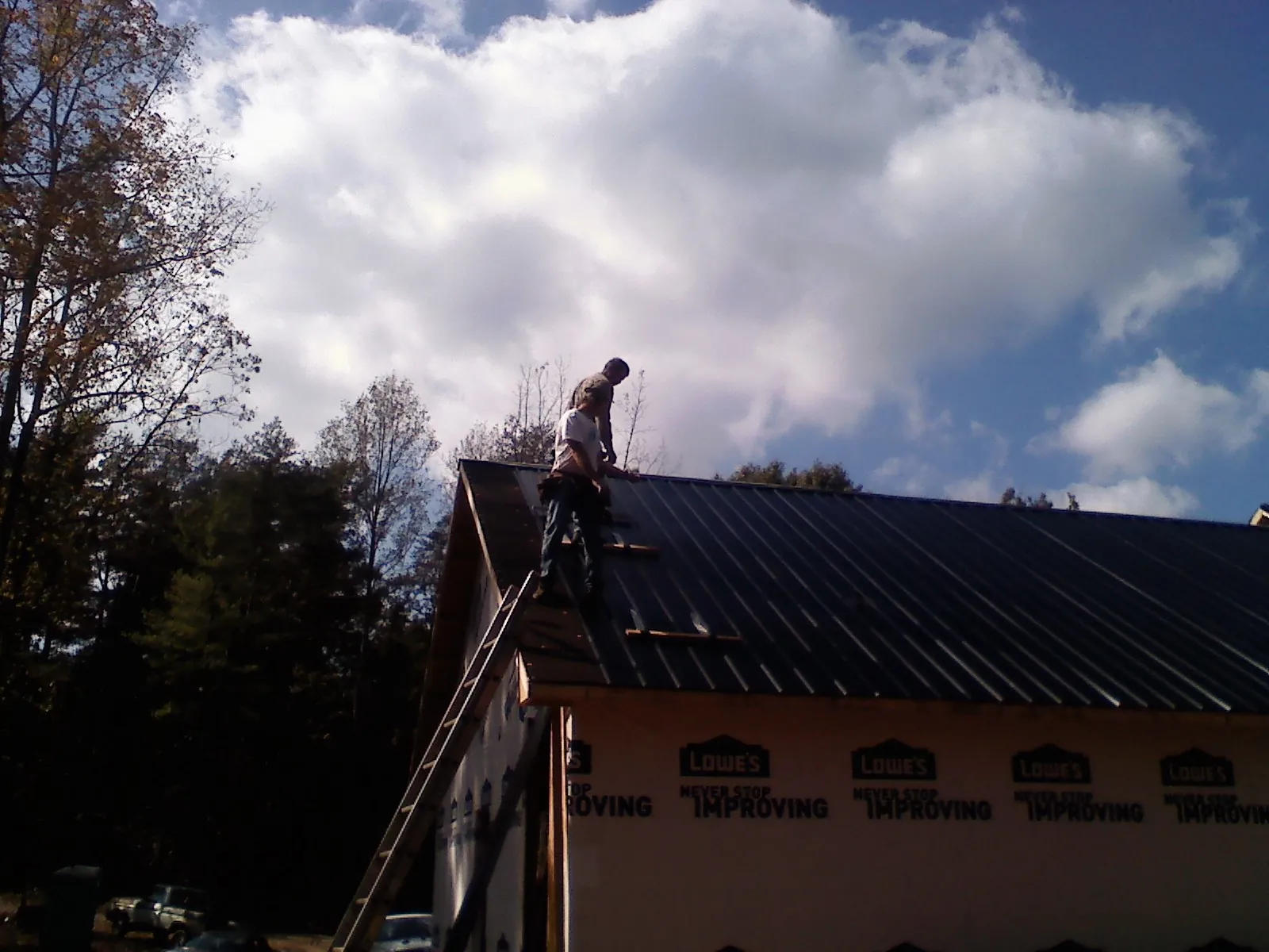 Roofer fastening dark metal panels high against a cloudy sky, from a Roof Inspection job in York Springs