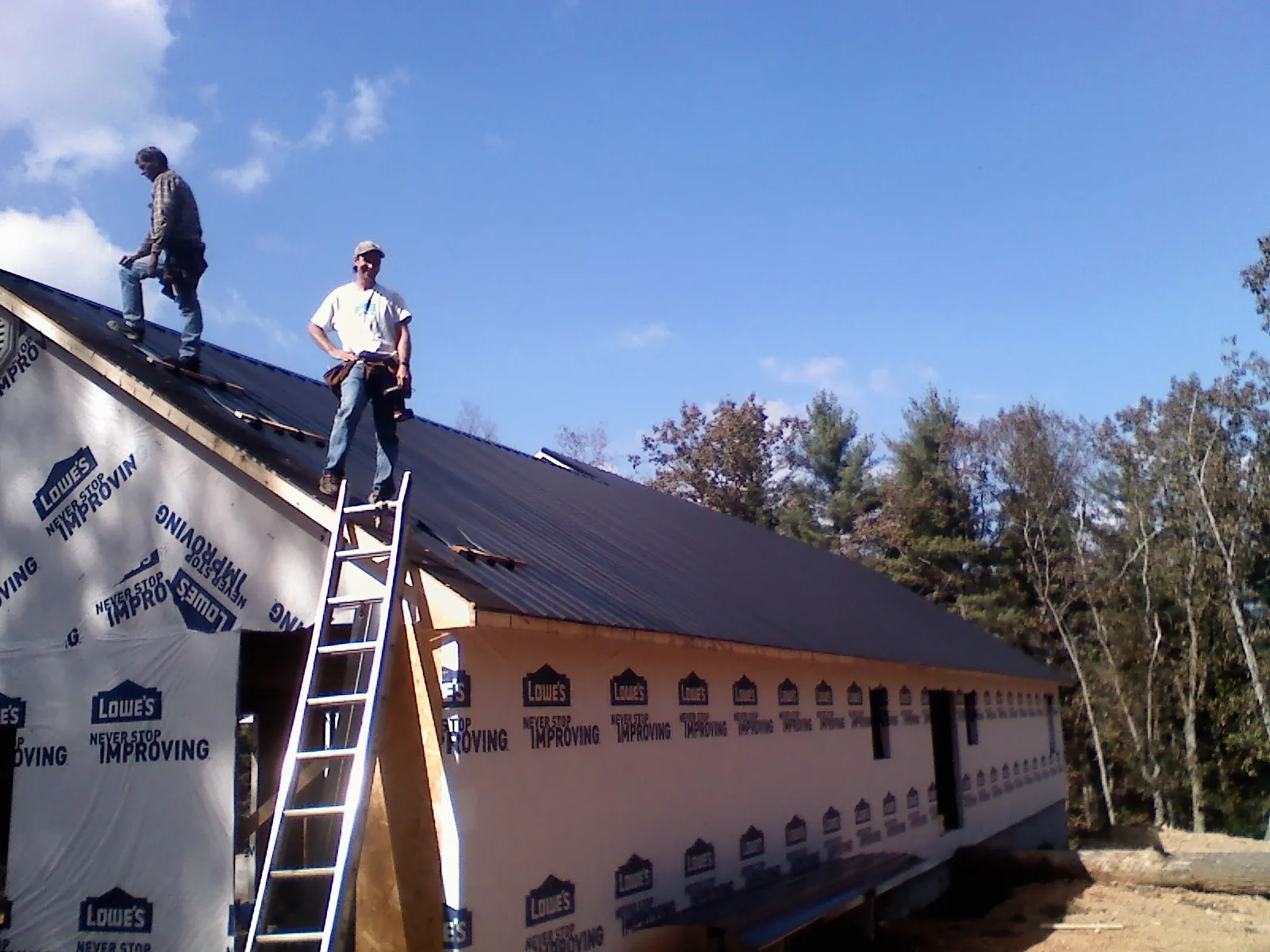 Two roofers standing on a long dark metal roof over a wrapped building in York Springs