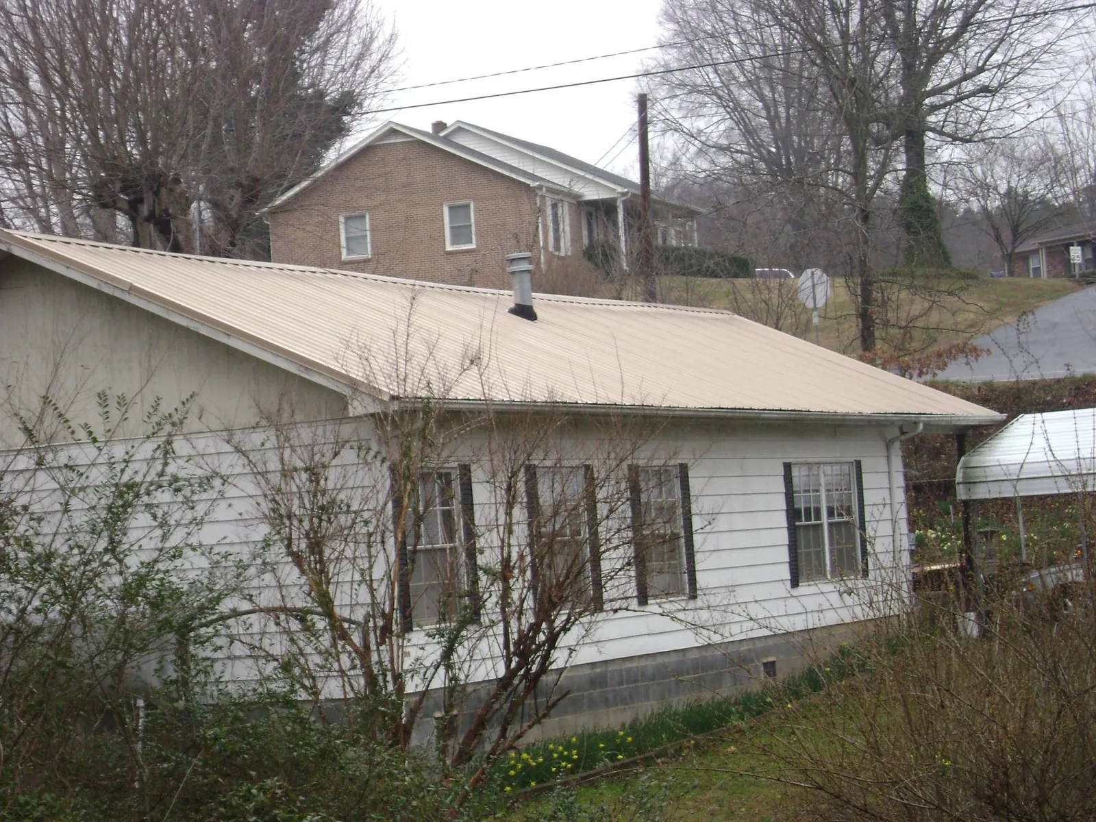 Tan metal roof on a white sided house set into a hillside — Commercial Roofing by Roofing Brothers in York Springs